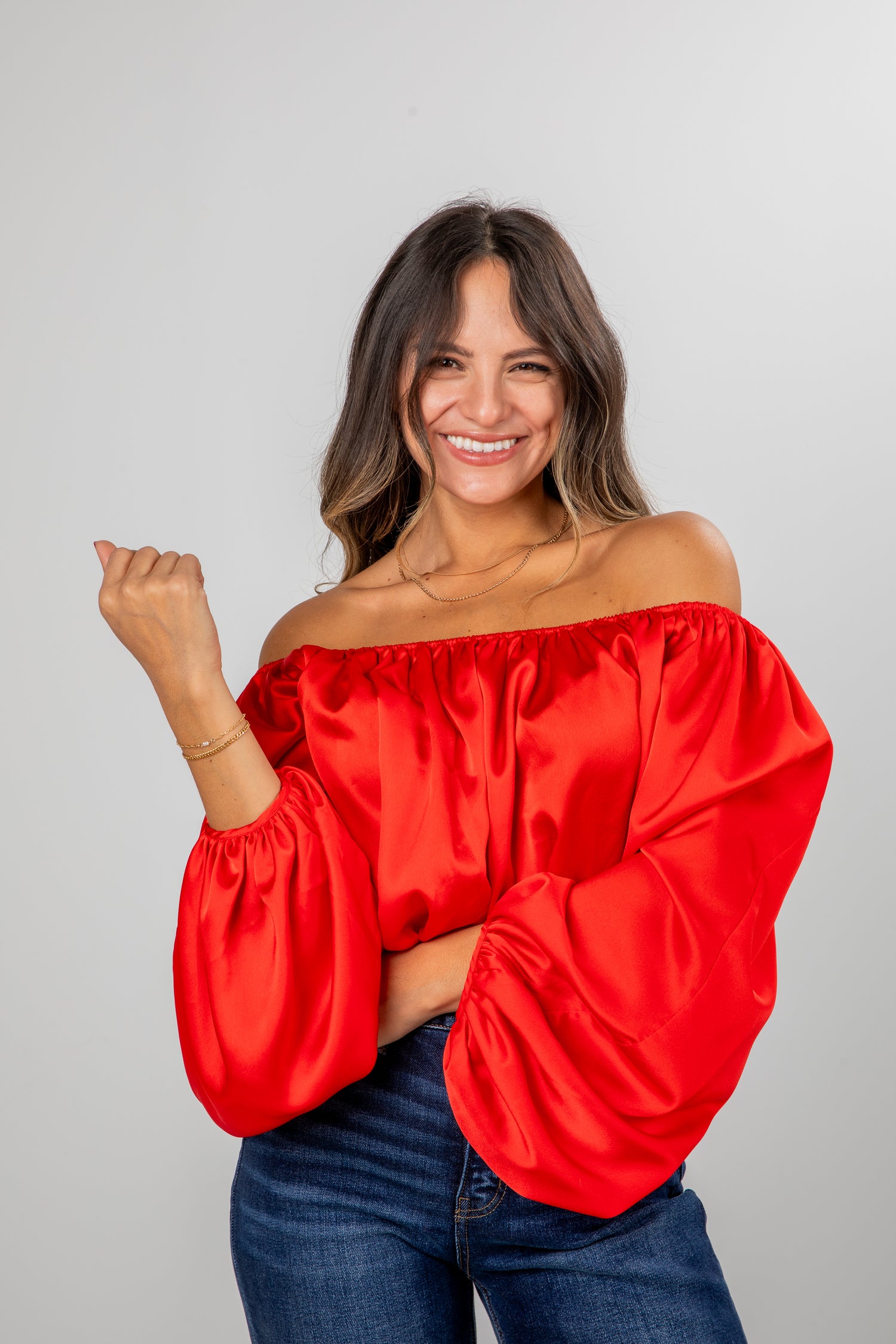 Woman wearing a red off-shoulder top against a gray background