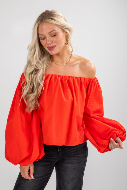 Woman wearing a bright red off-shoulder top with black pants on a white background