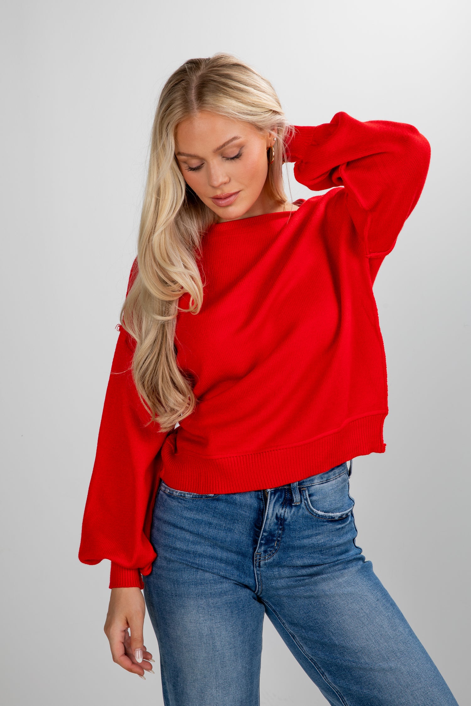 Woman wearing a red sweater and blue jeans on a plain background