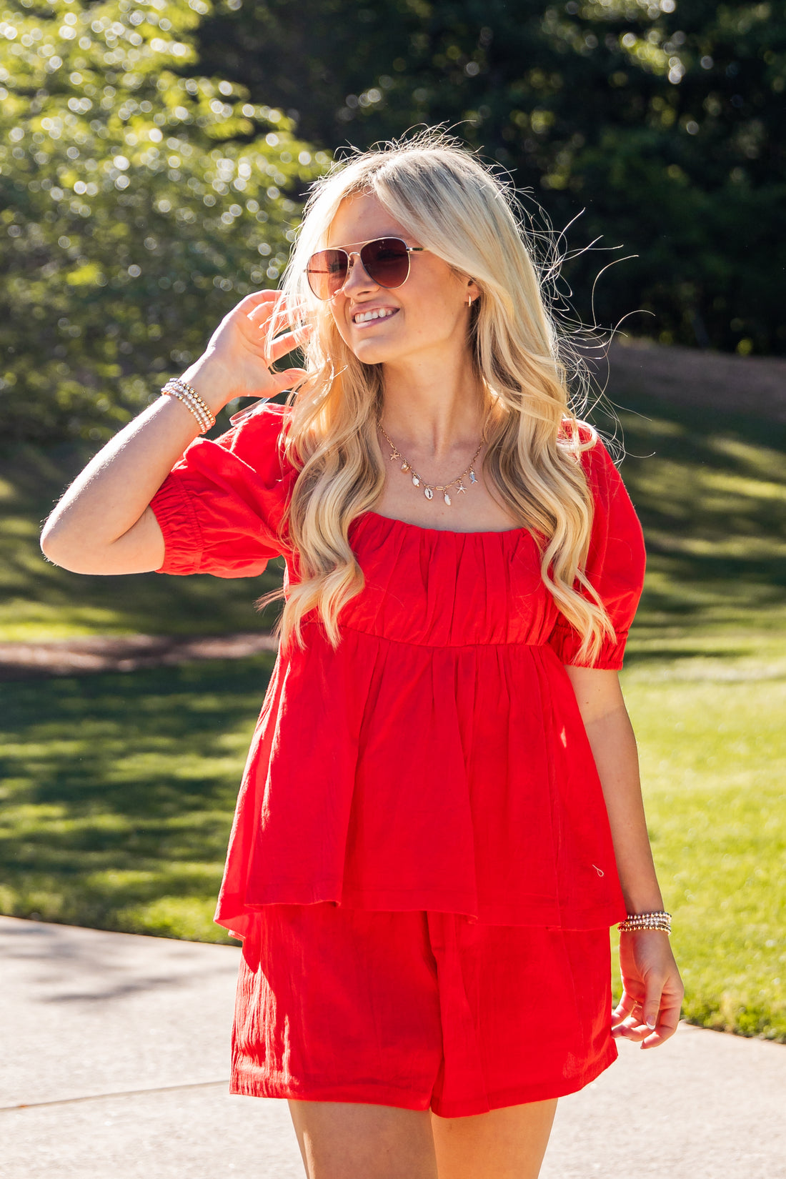 Woman in a red outfit standing outdoors with greenery in the background