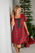 Woman in a red plaid dress standing next to a Christmas tree with presents.