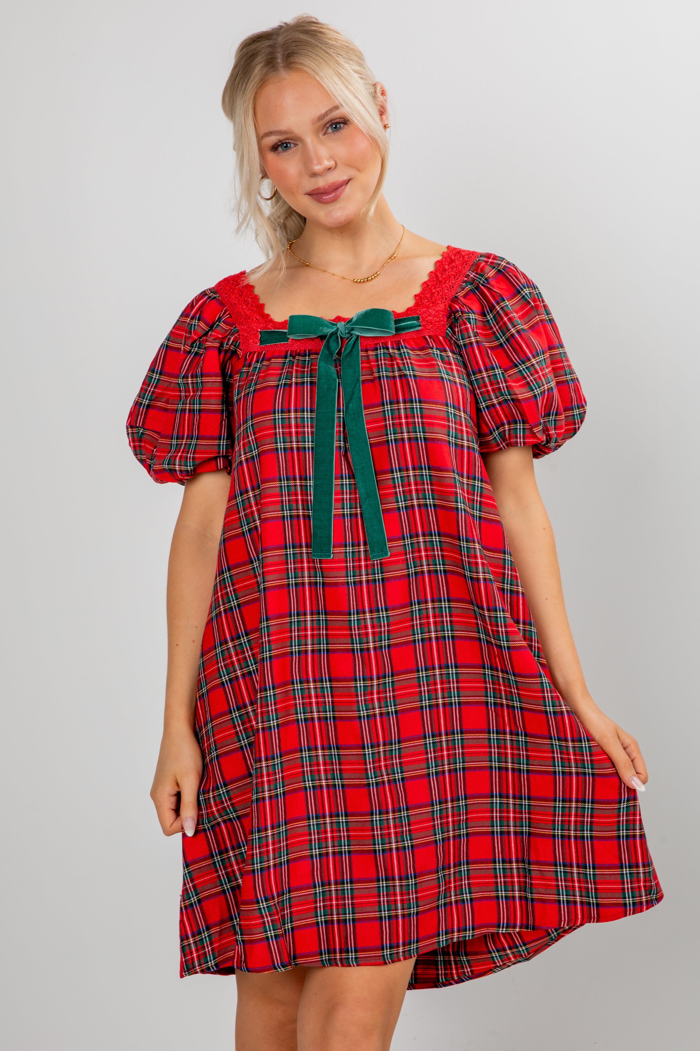 Woman wearing a red plaid dress with green accents on a gray background