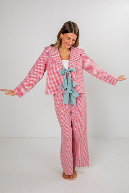 Woman wearing a pink checkered pajama set with a blue bow on a white background