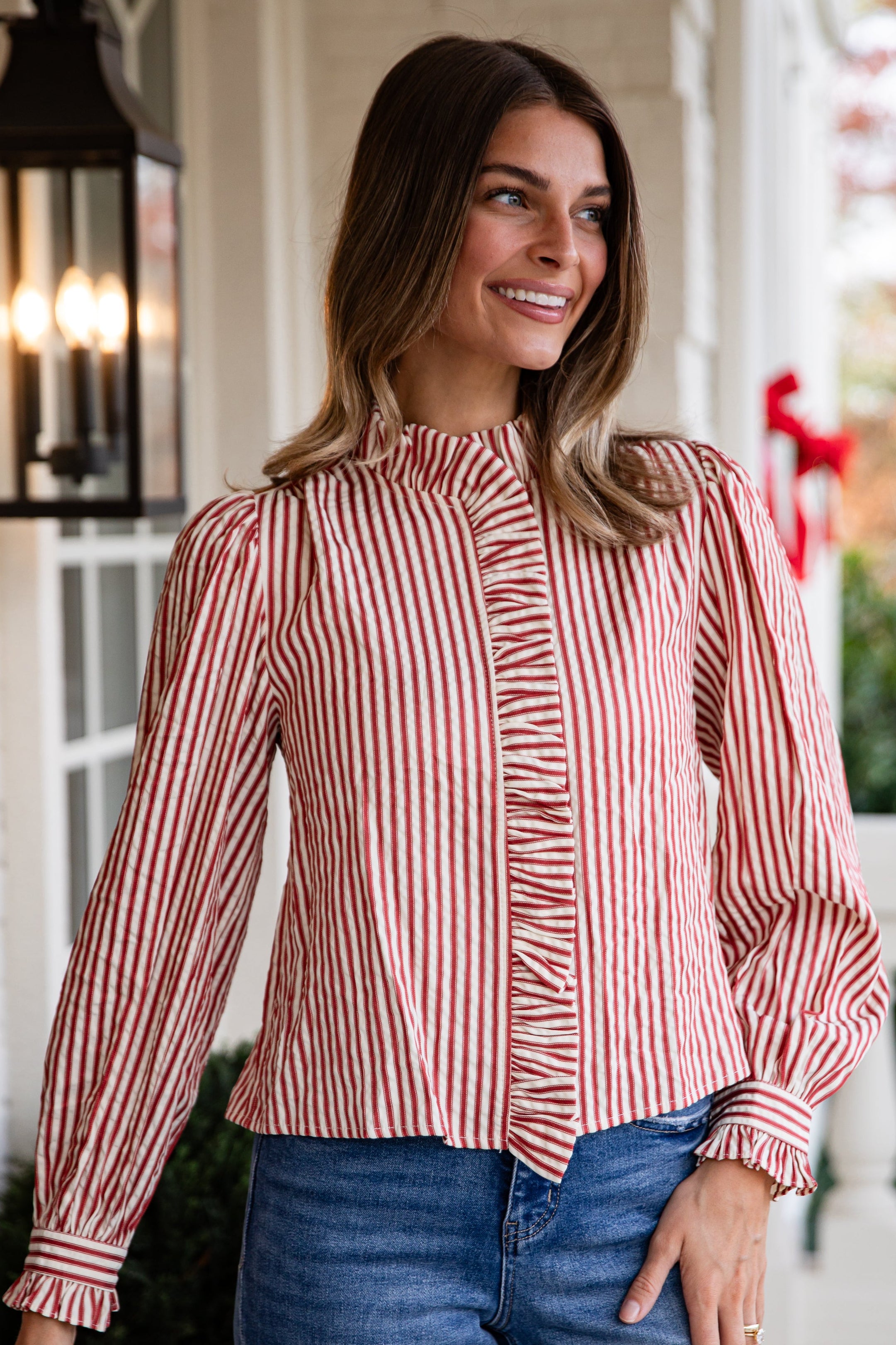 Woman wearing a red and white striped blouse and blue jeans standing on a porch.