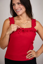 Woman wearing a red sleeveless top with ruffled details against a plain background