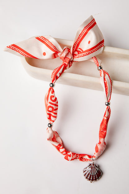 Necklace with red and white patterned band and shell pendant on a white background