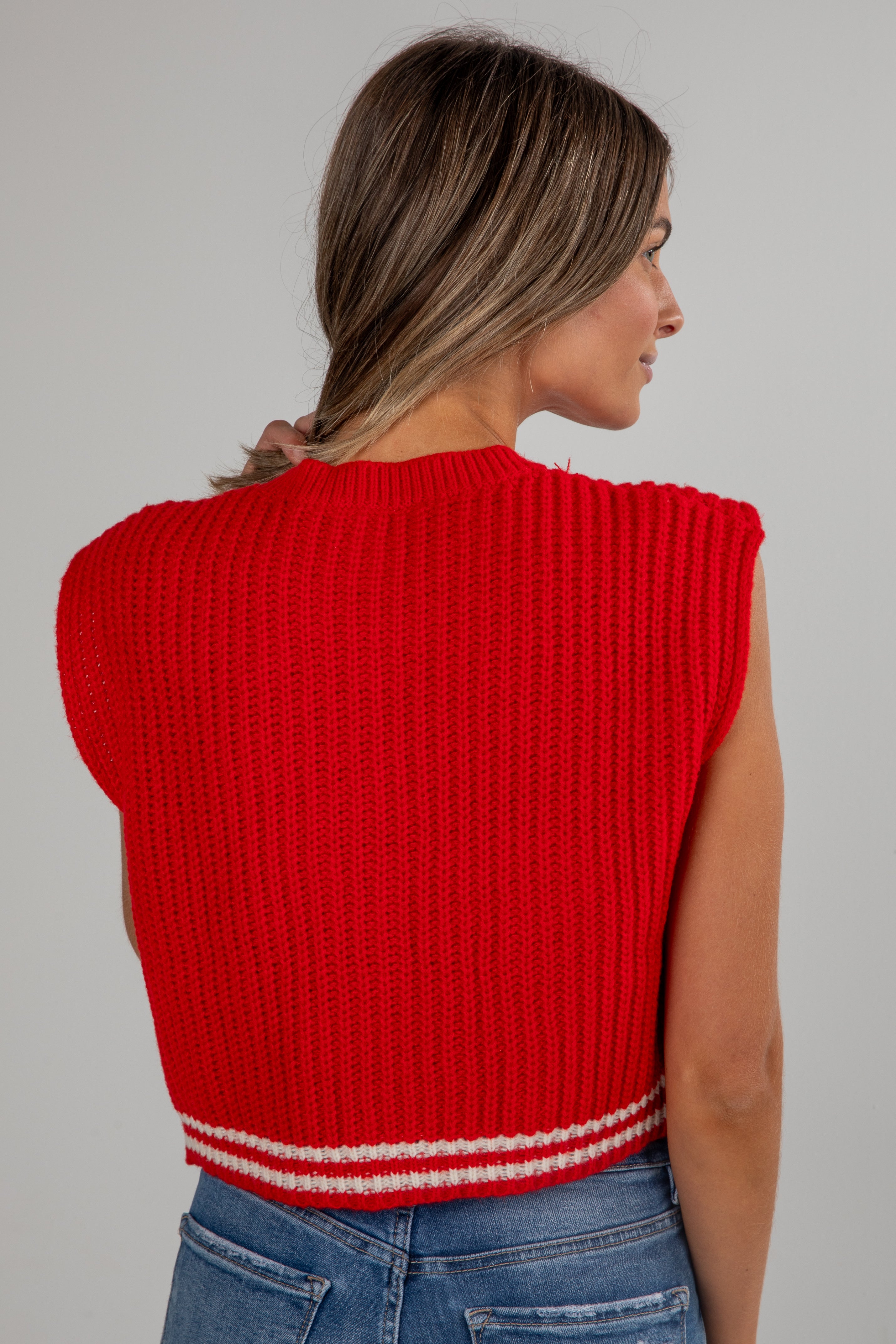 Woman wearing a red ribbed sleeveless sweater against a gray background