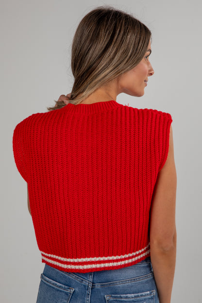 Woman wearing a red ribbed sleeveless sweater against a gray background