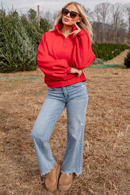 Woman in a red sweatshirt and blue jeans standing in a field with trees in the background