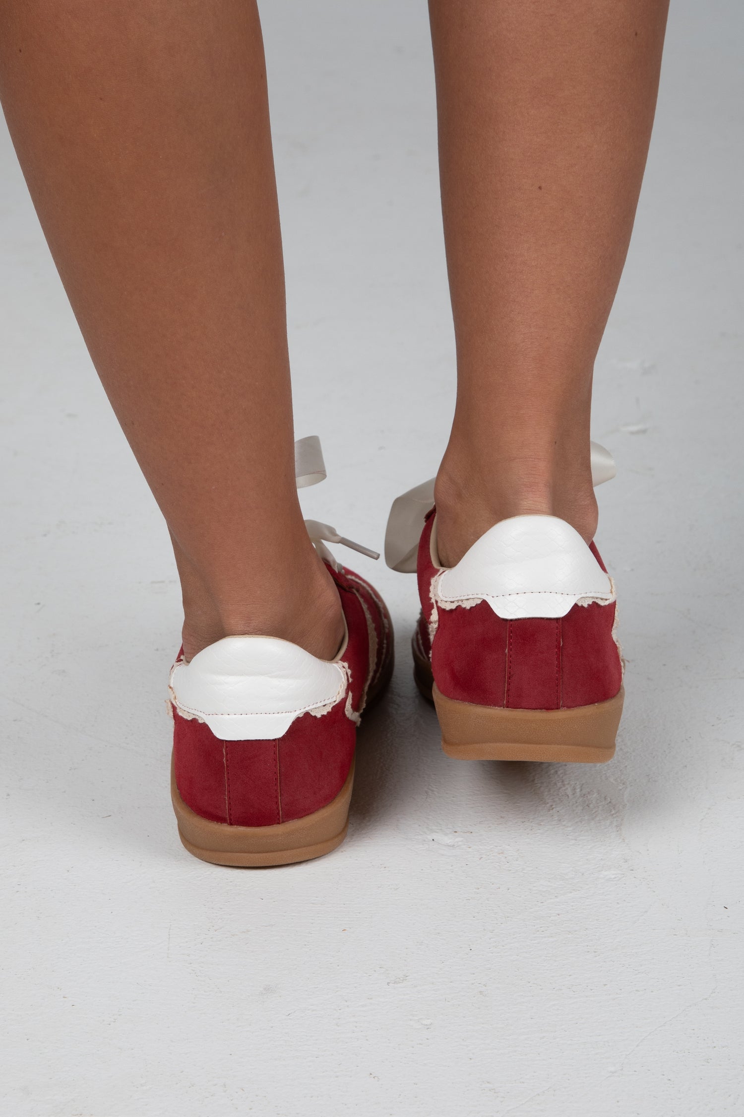 Red shoes with white soles worn by a person on a light gray background