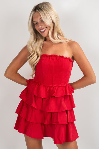 Woman wearing a red strapless dress with ruffled layers on a plain background