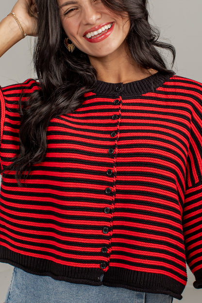 A woman wearing a cropped knit cardigan sweater with horizontal red and black stripes, black buttons down the front, and a black ribbed crew neck, cuffs, and hem.