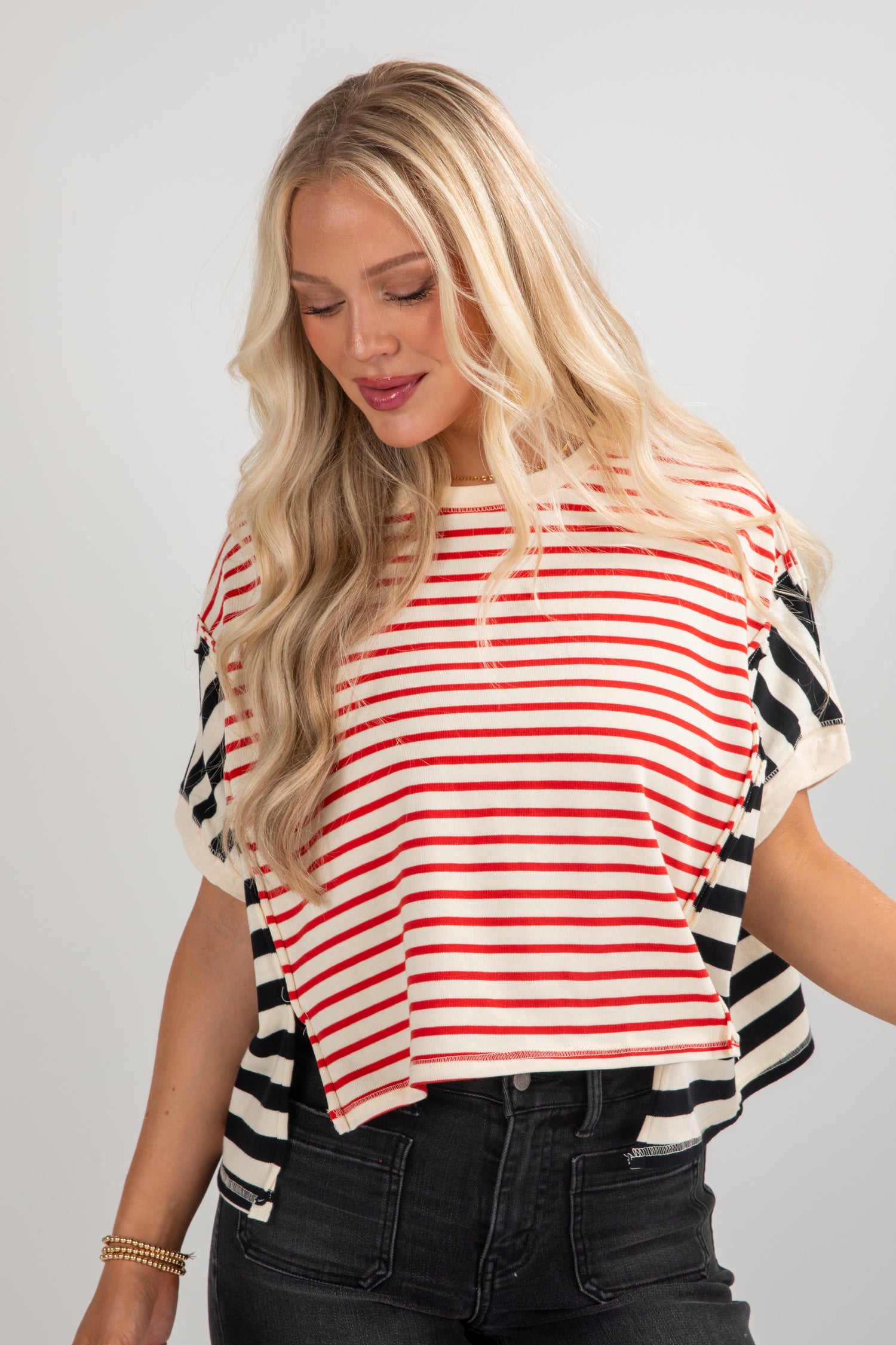 Woman wearing a red and white striped shirt with black and white patterned sleeves on a gray background