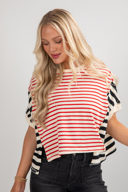 Woman wearing a red and white striped shirt with black and white patterned sleeves on a gray background