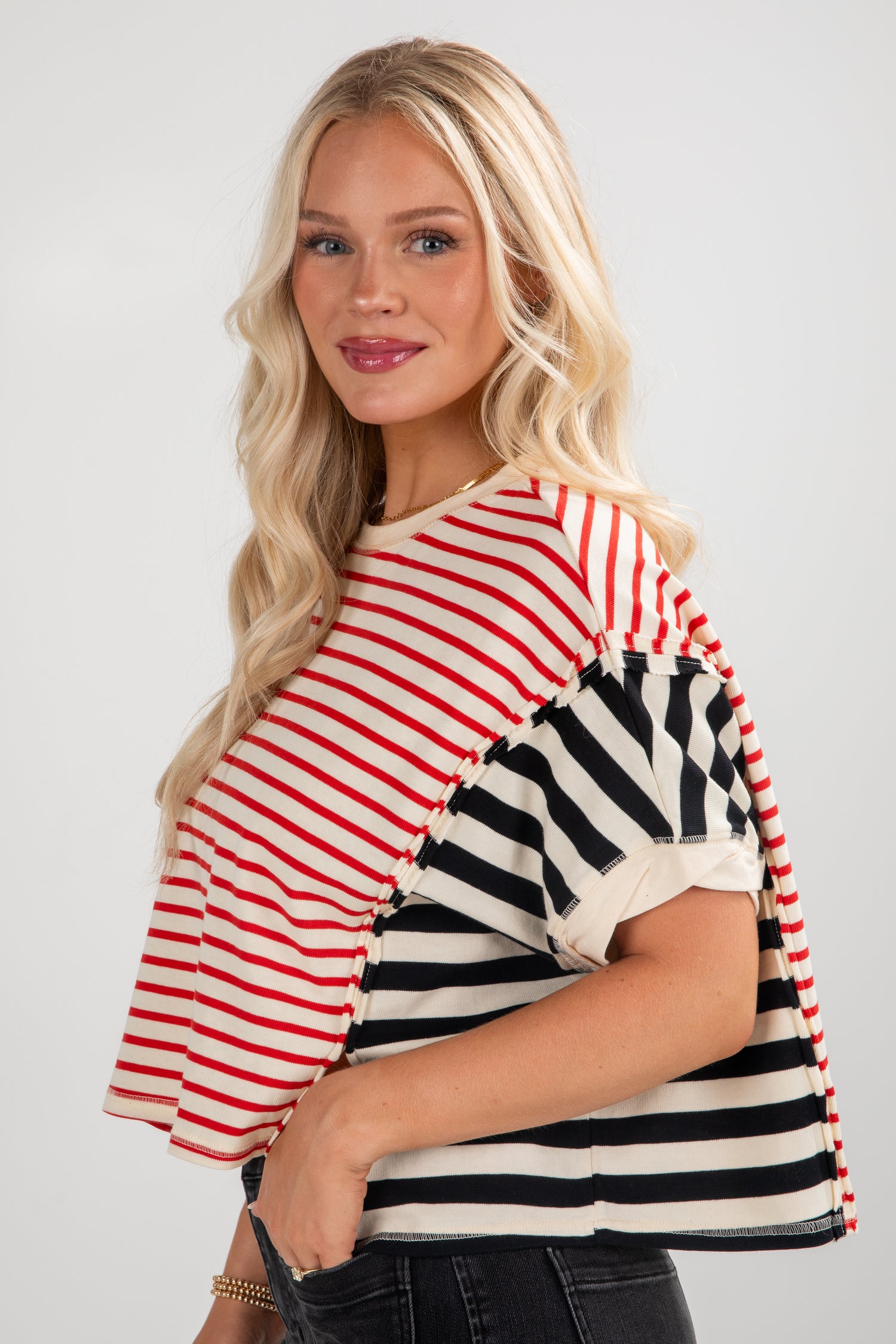 Woman wearing a striped top with red, black, and white pattern on a plain background