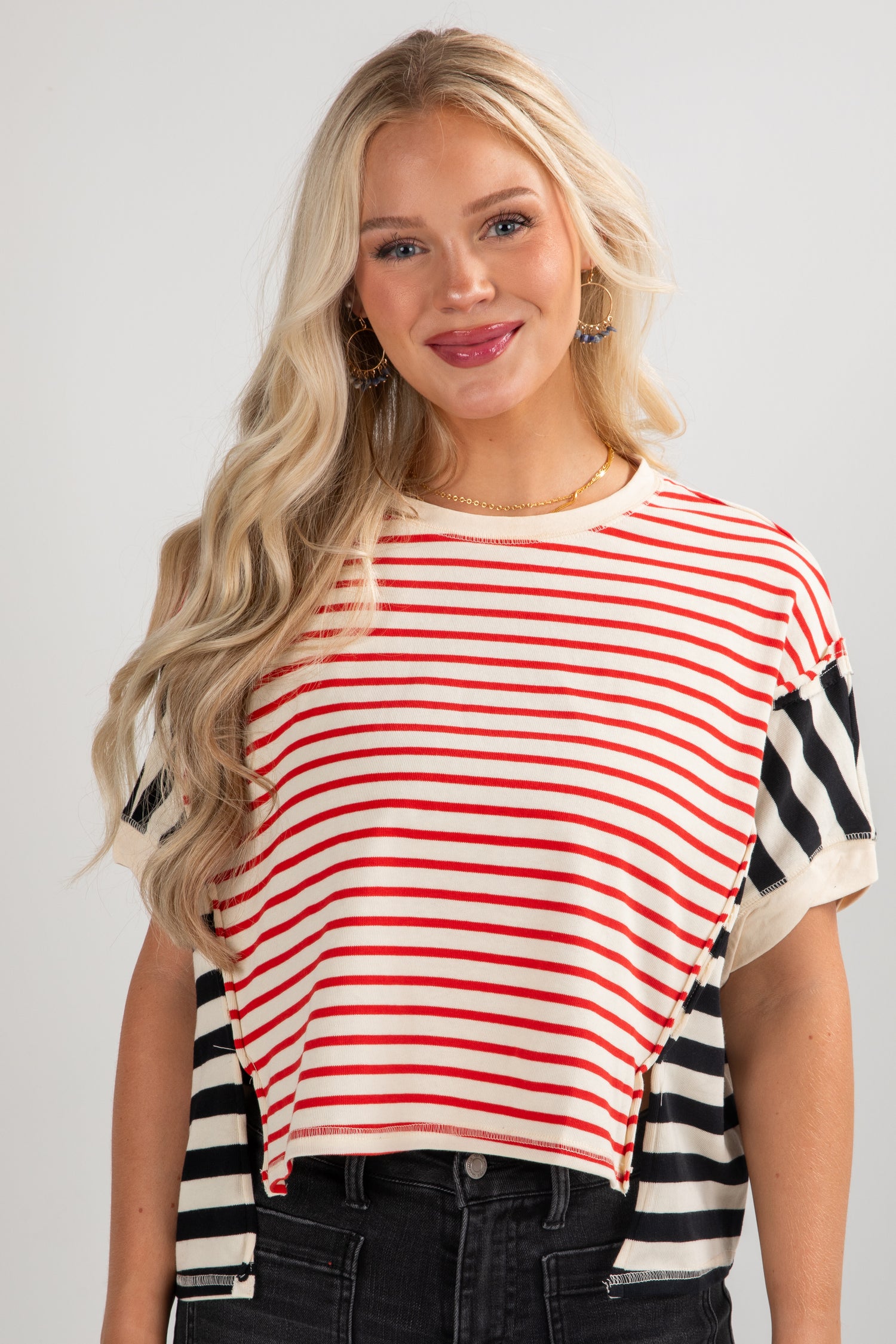 Woman wearing a red and white striped top with black and white striped sleeves on a plain background