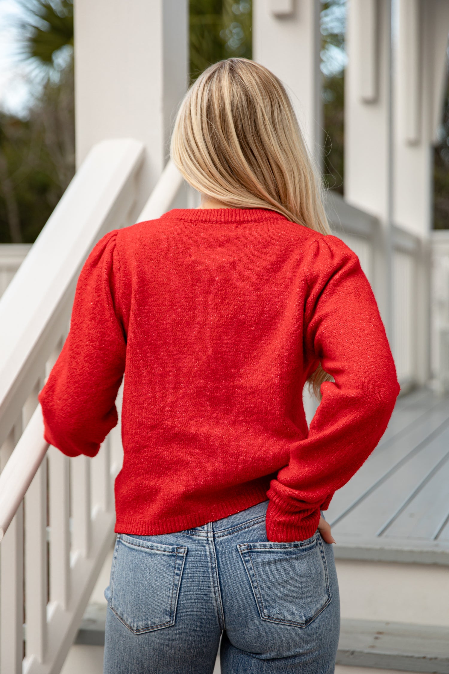 Person wearing a red sweater and blue jeans standing on a porch.