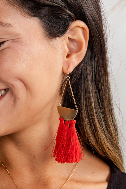 Close-up of a woman wearing a red tassel earring with a gold half-circle design.