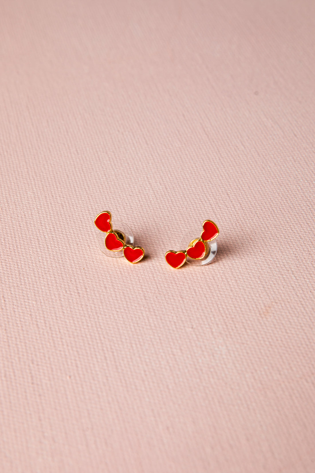 Pair of red heart-shaped earrings on a pink background