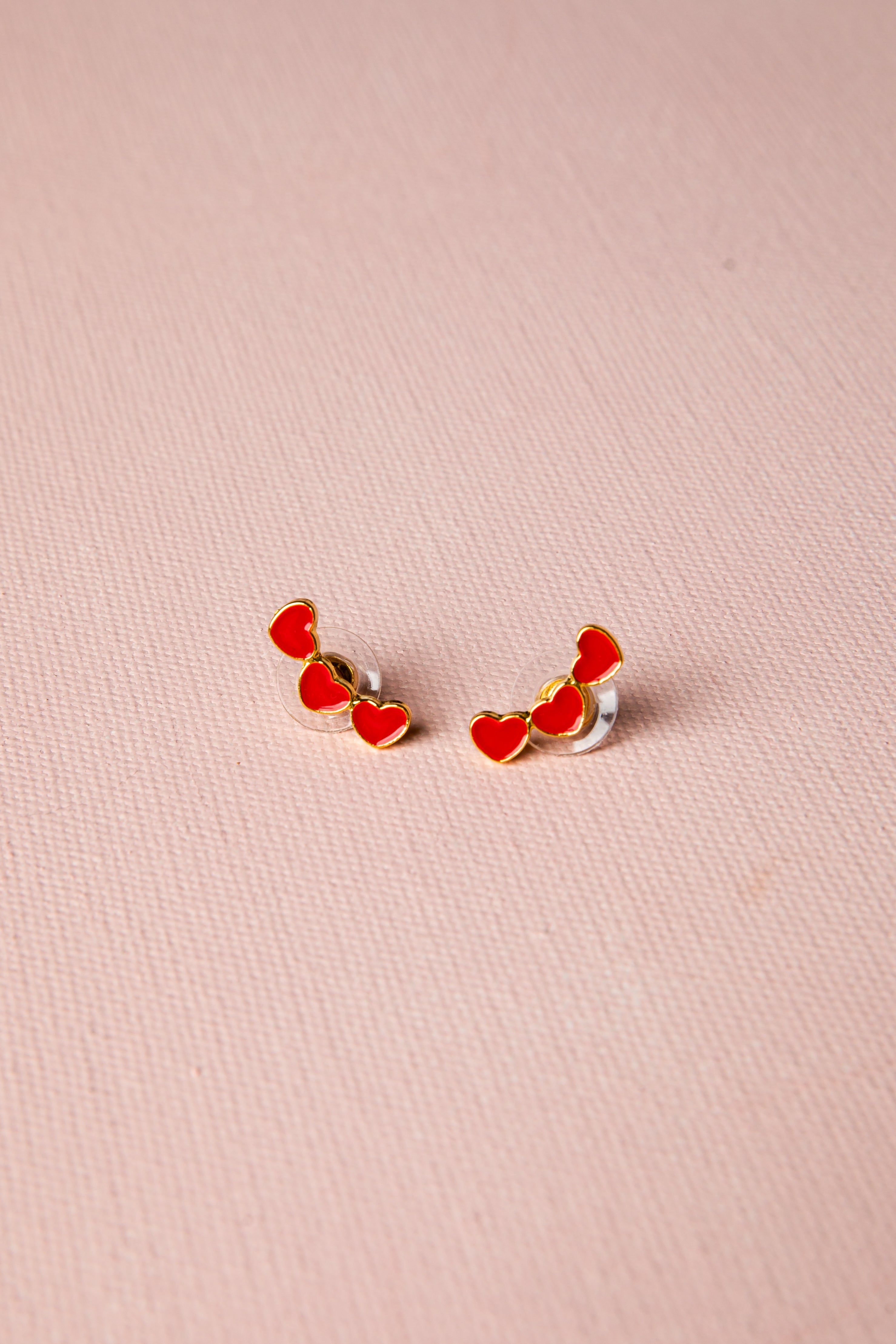 Pair of red heart-shaped earrings on a pink background
