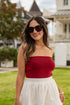 Woman wearing a red top and white skirt with sunglasses outdoors.