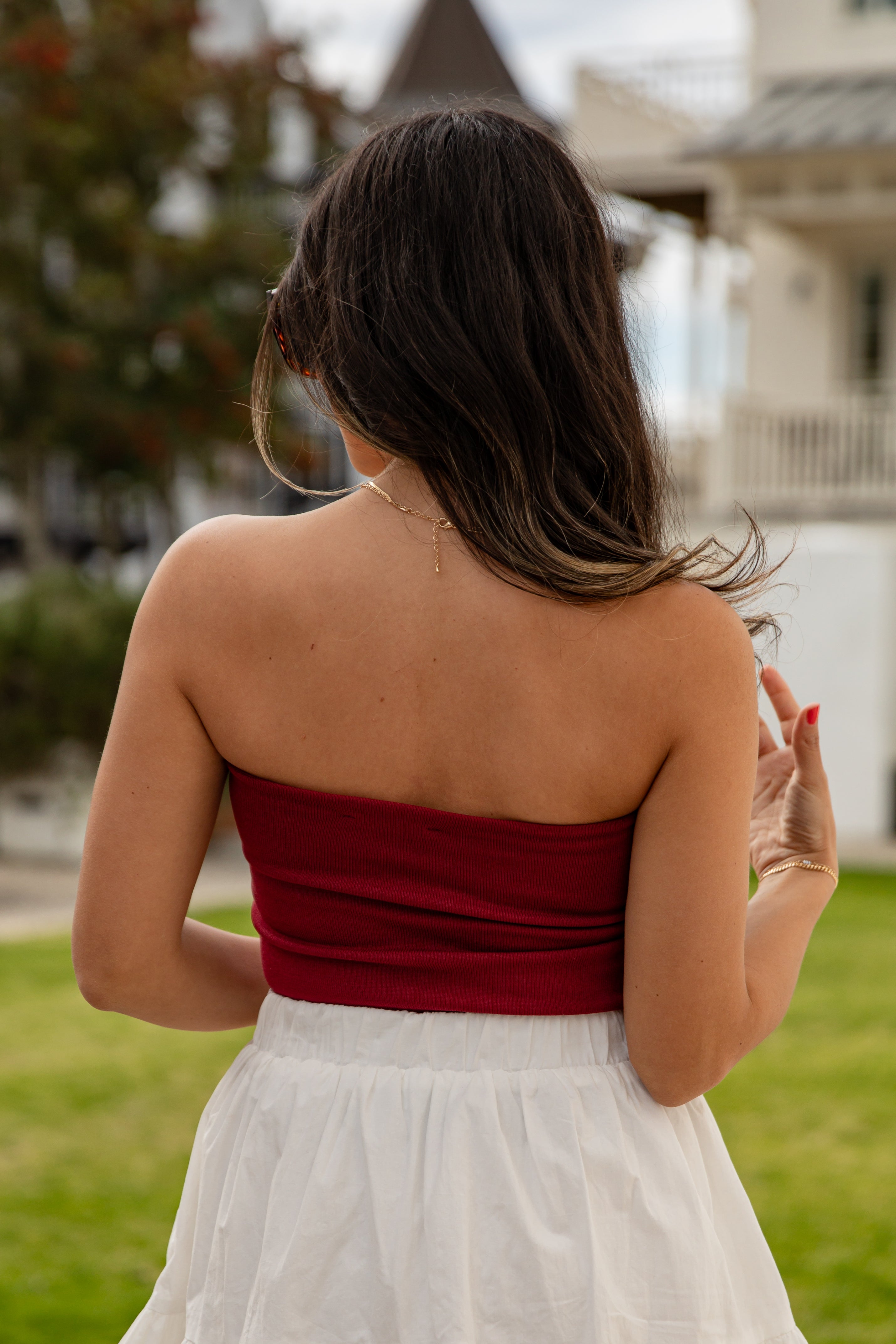 Woman in a red top and white skirt standing outdoors with blurred background