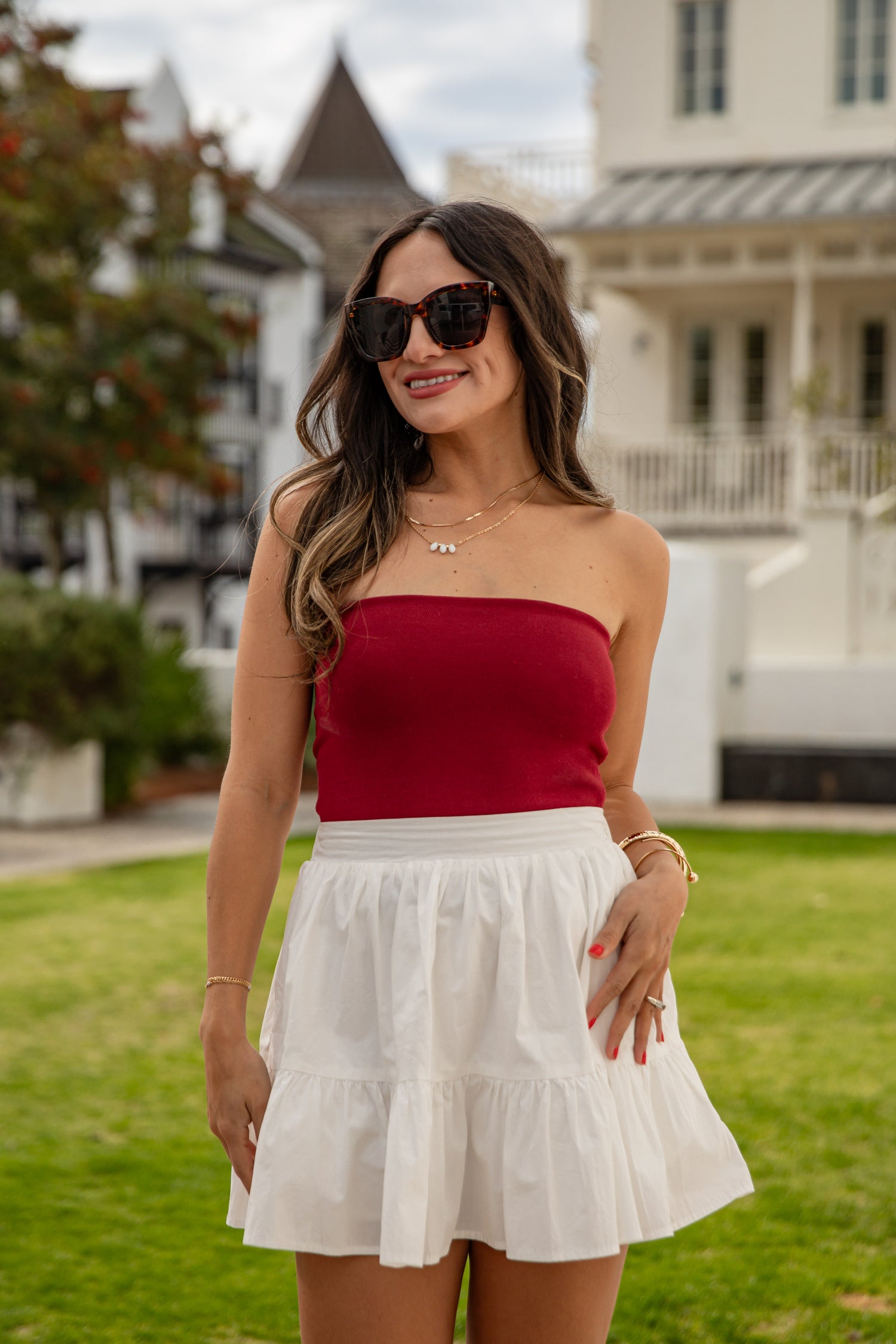 Woman wearing a red top and white skirt outdoors with a house in the background