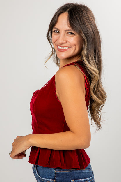 Woman wearing a red sleeveless top with a peplum waist on a plain background