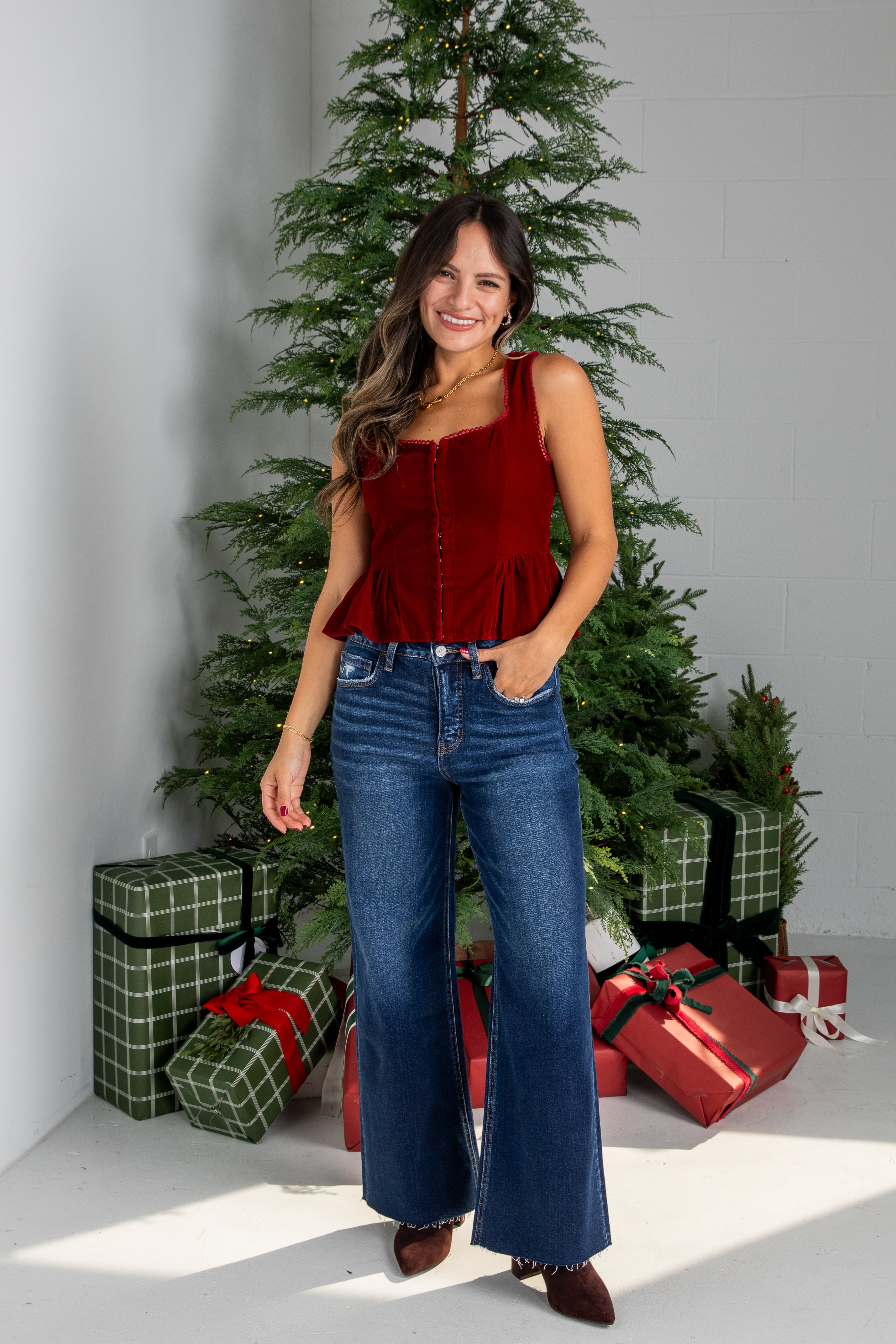 Woman in a red top and blue jeans standing in front of a Christmas tree with presents.