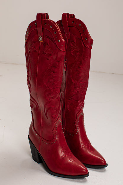 A pair of red leather cowboy boots with western embroidery, studded details, and low block heels, photographed on a light gray studio background.