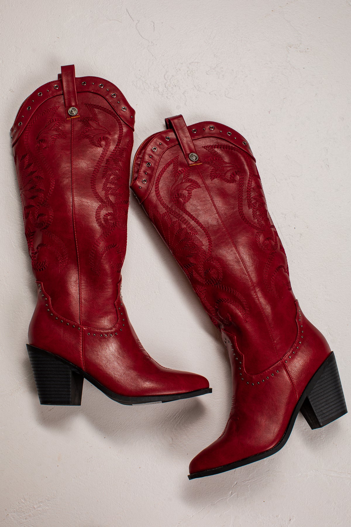 A pair of red leather cowboy boots with black block heels, shown from a top-down angle on a textured off-white background.