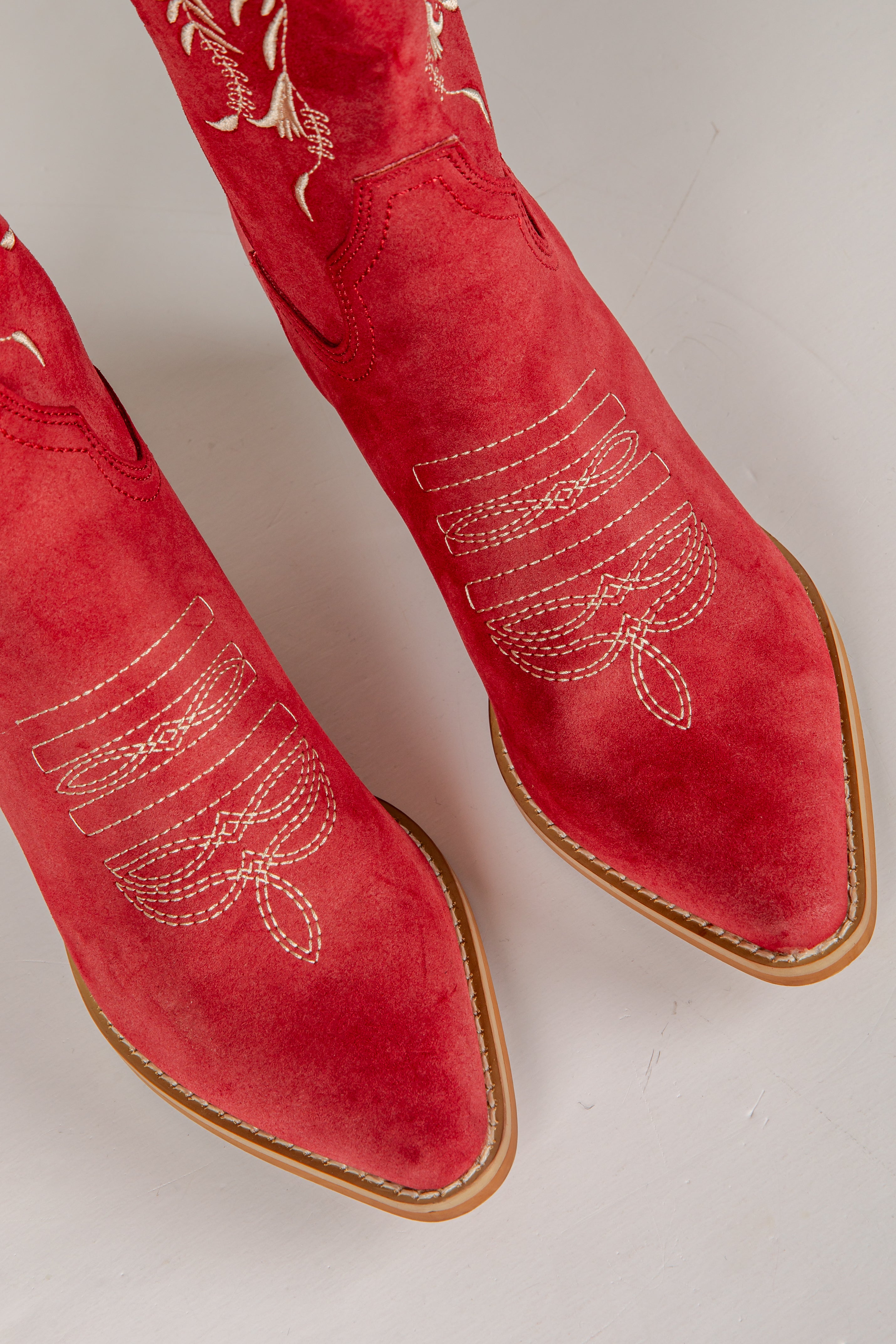 Red suede boots with gold embroidery on a light gray background
