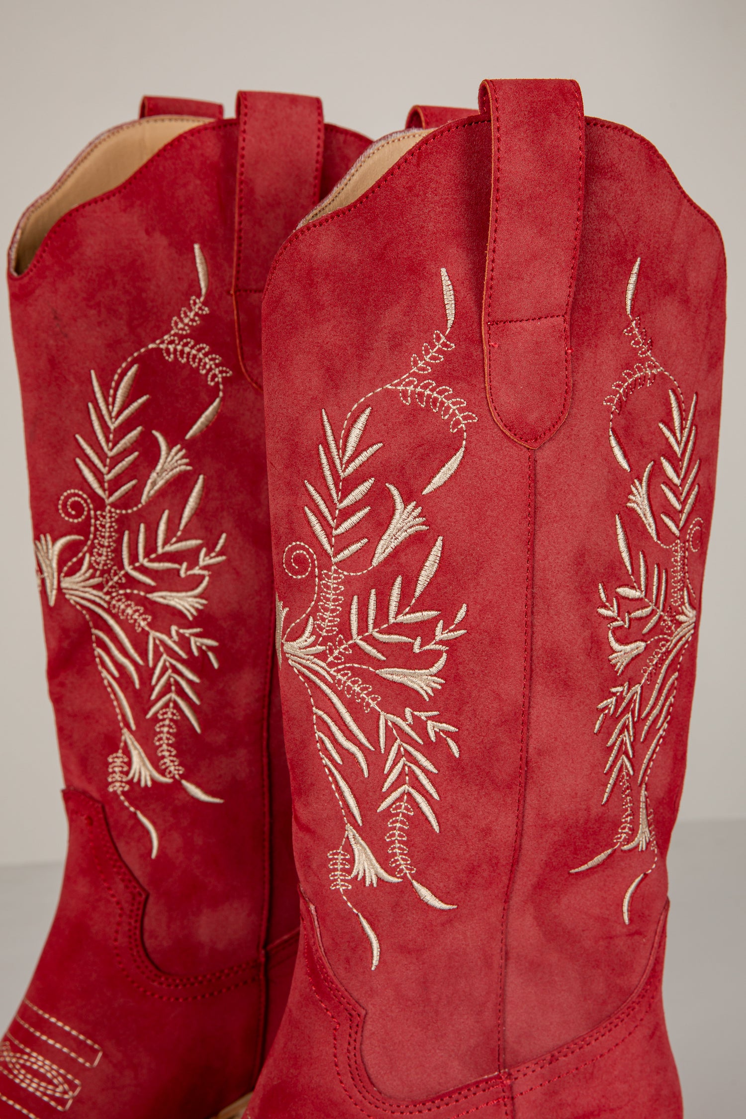 Red boots with white floral embroidery on a light gray background