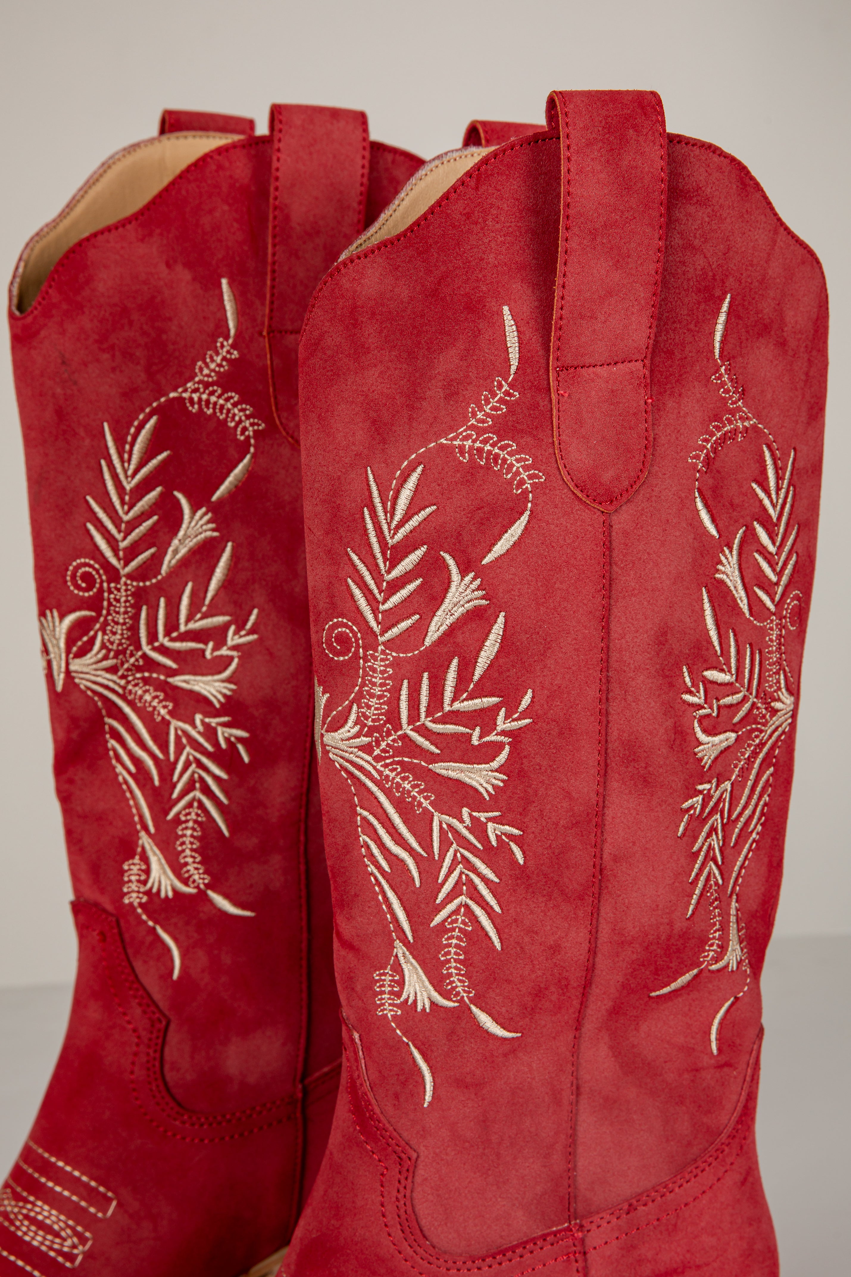 Red boots with white floral embroidery on a light gray background
