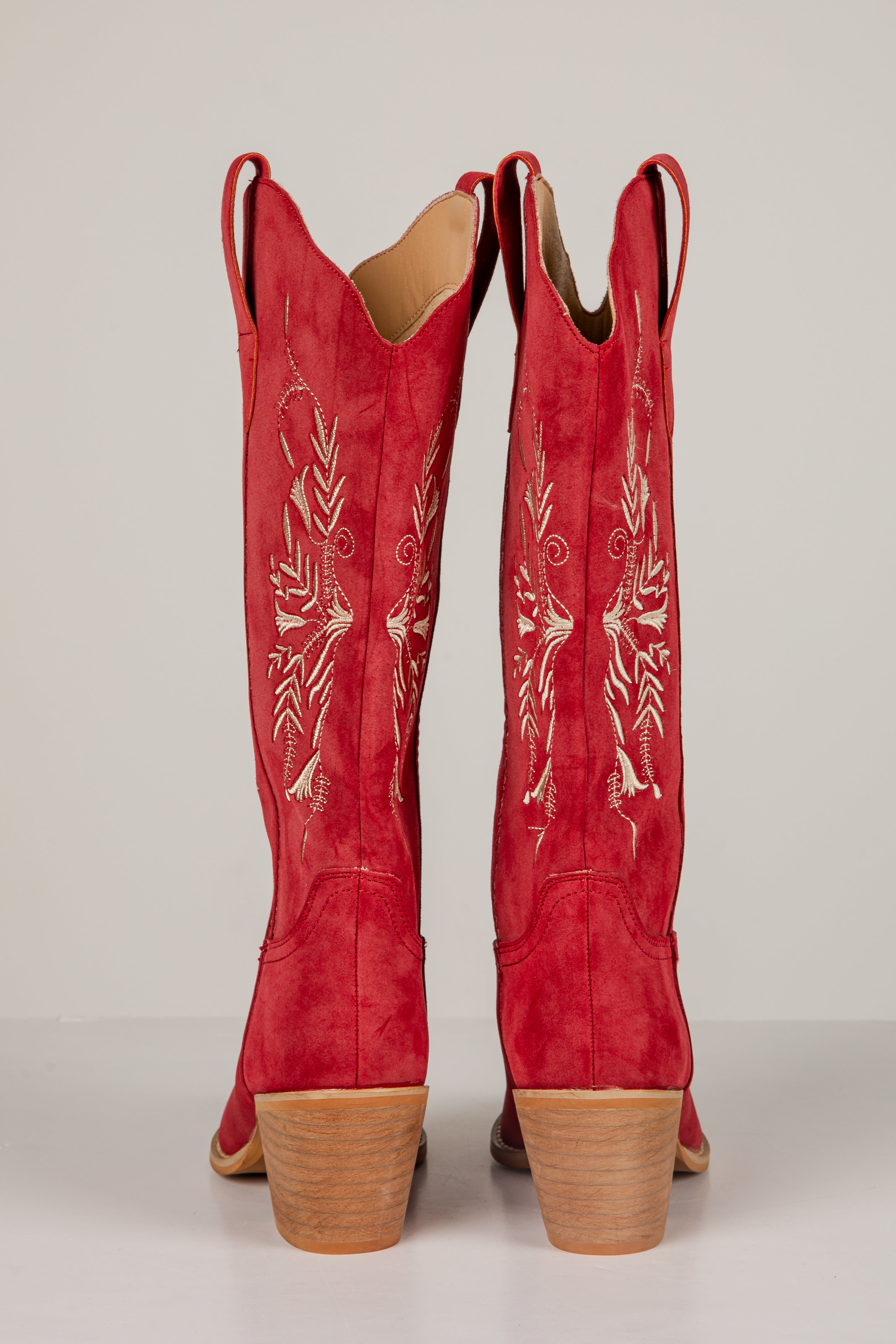 Red cowboy boots with white embroidery on a light gray background