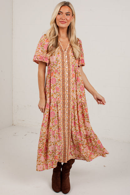 A woman modeling a bohemian-style midi dress with a pink and orange floral print, featuring a beige lace-trimmed V-neckline and short flutter sleeves, paired with brown boots against a white studio background.