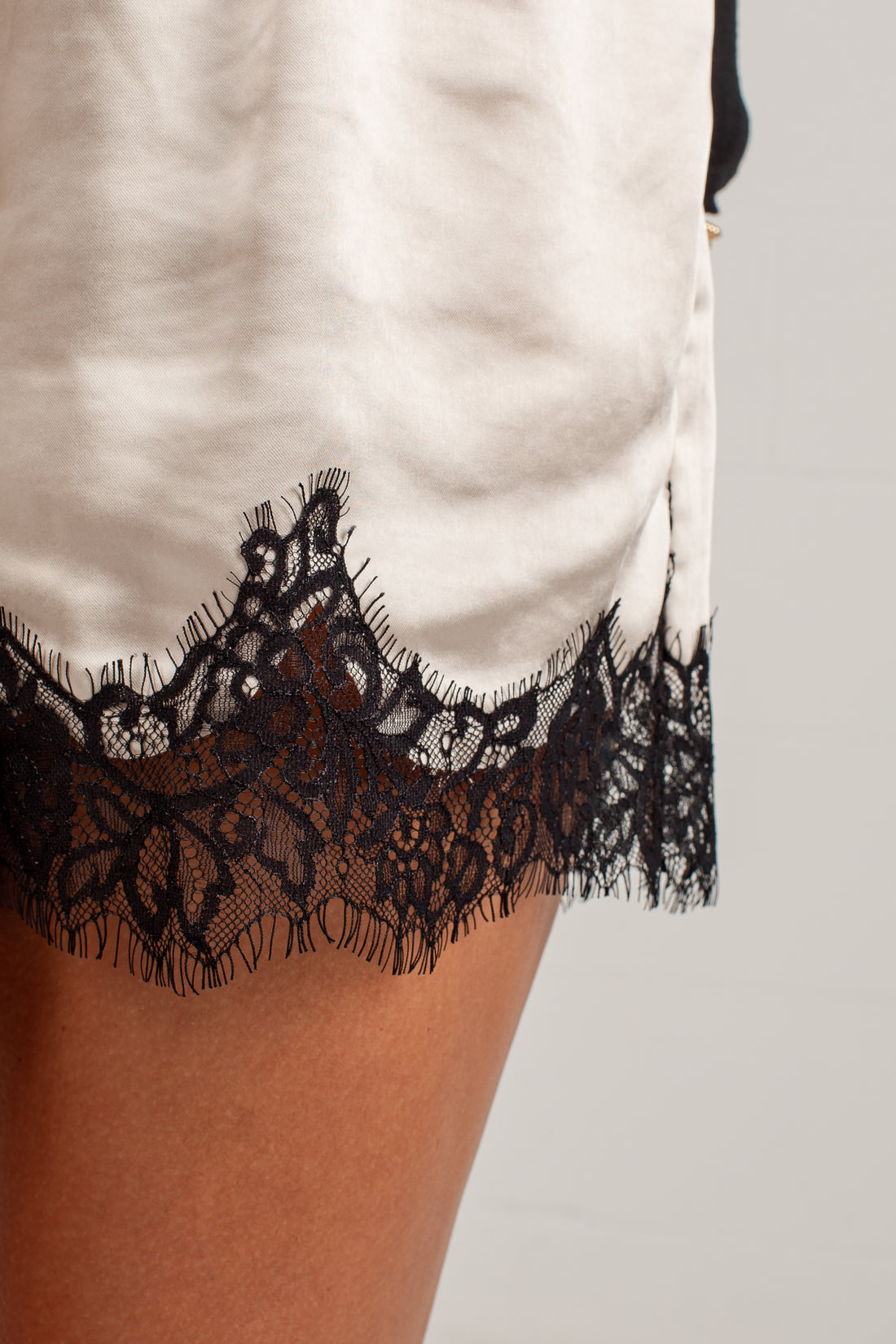 Close-up of a white satin or silk slip dress with a black lace hem, worn by a model.