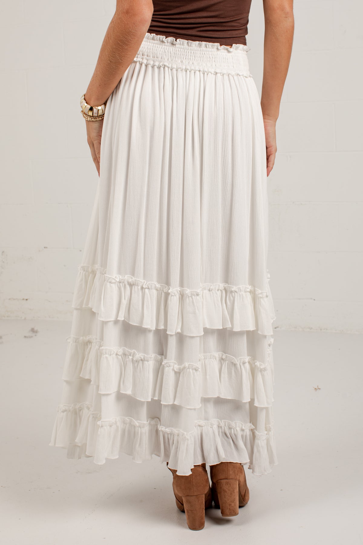 A white tiered maxi skirt with a smocked elastic waistband, shown on a model from the back against a light gray studio background.