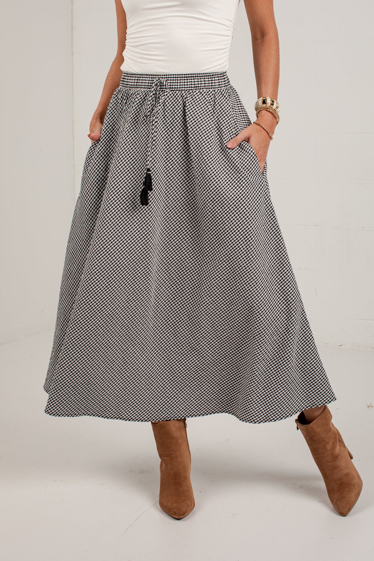 A woman wearing a high-waisted, A-line midi skirt with a small black and white micro-pattern, paired with a white top and brown suede ankle boots.