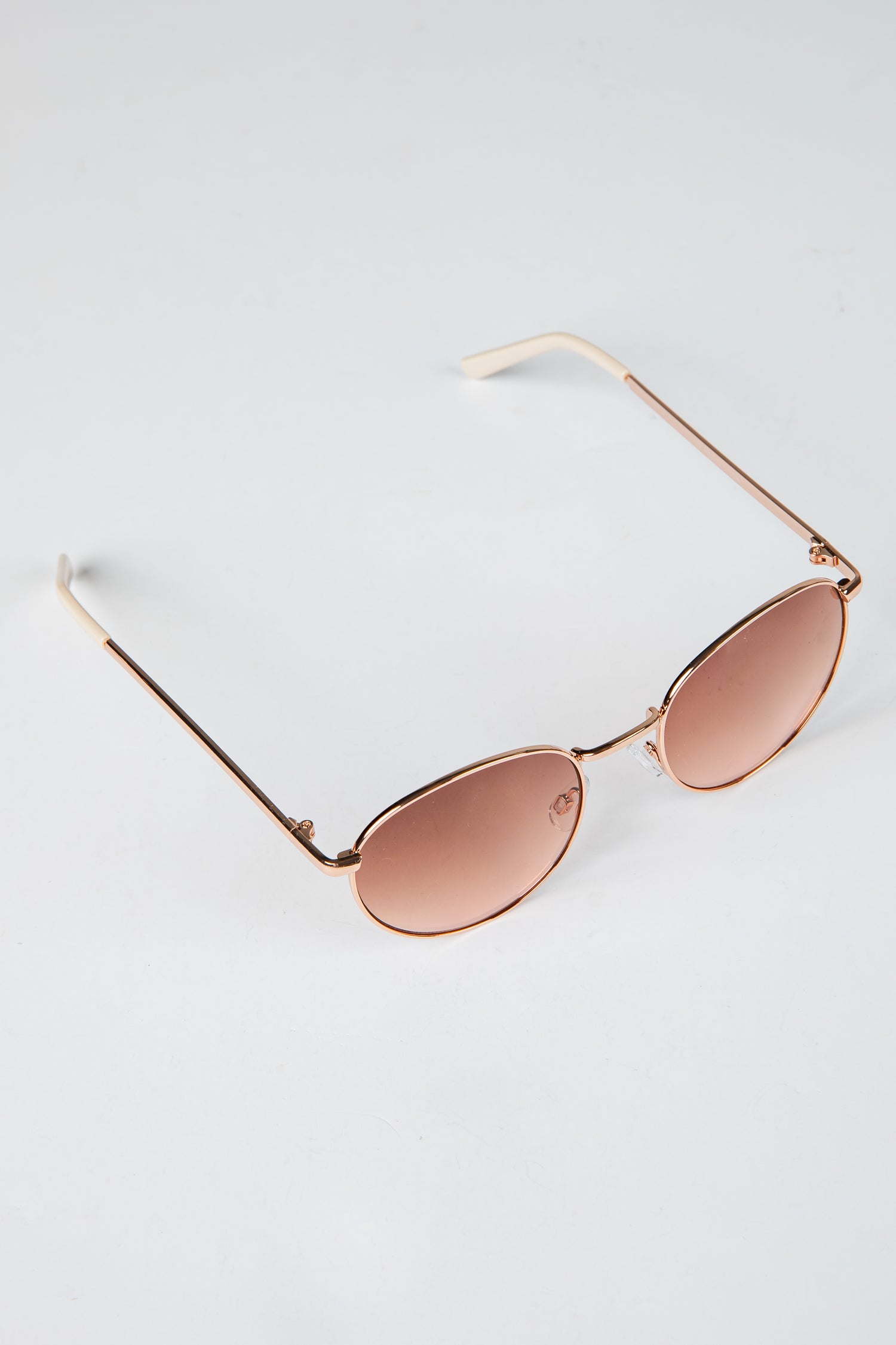 Rose gold sunglasses with pink lenses on a light gray background