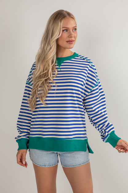 Woman wearing a blue and white striped sweater with green trim on a plain background