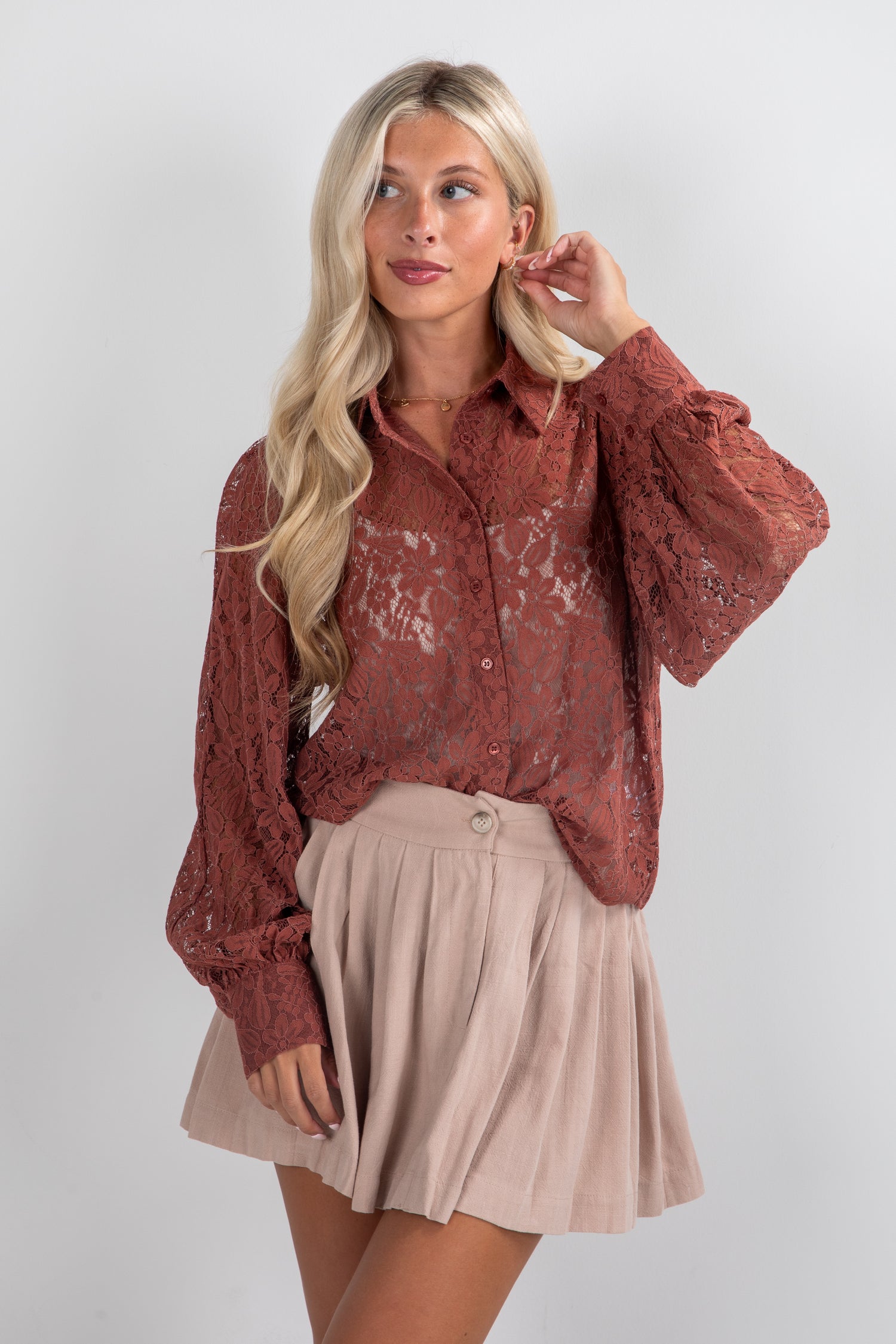 Woman wearing a rust-colored lace blouse and beige skirt on a white background