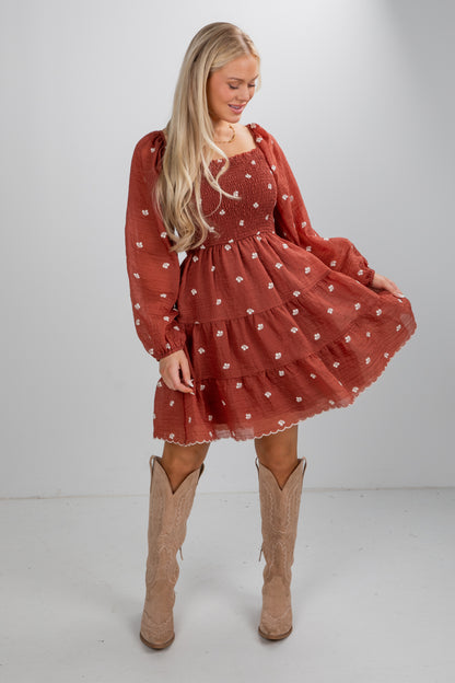 Woman wearing a rust-colored dress with long sleeves and cut-out knee-high boots on a white background