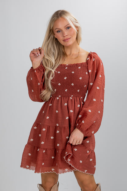 Woman wearing a rust-colored dress with floral pattern on a white background