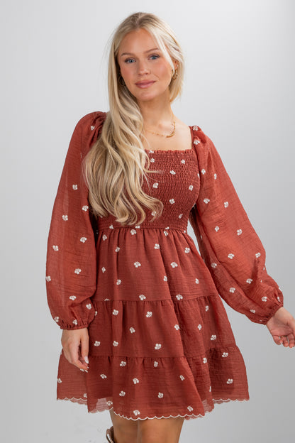 Woman wearing a rust-colored dress with long sleeves on a plain background