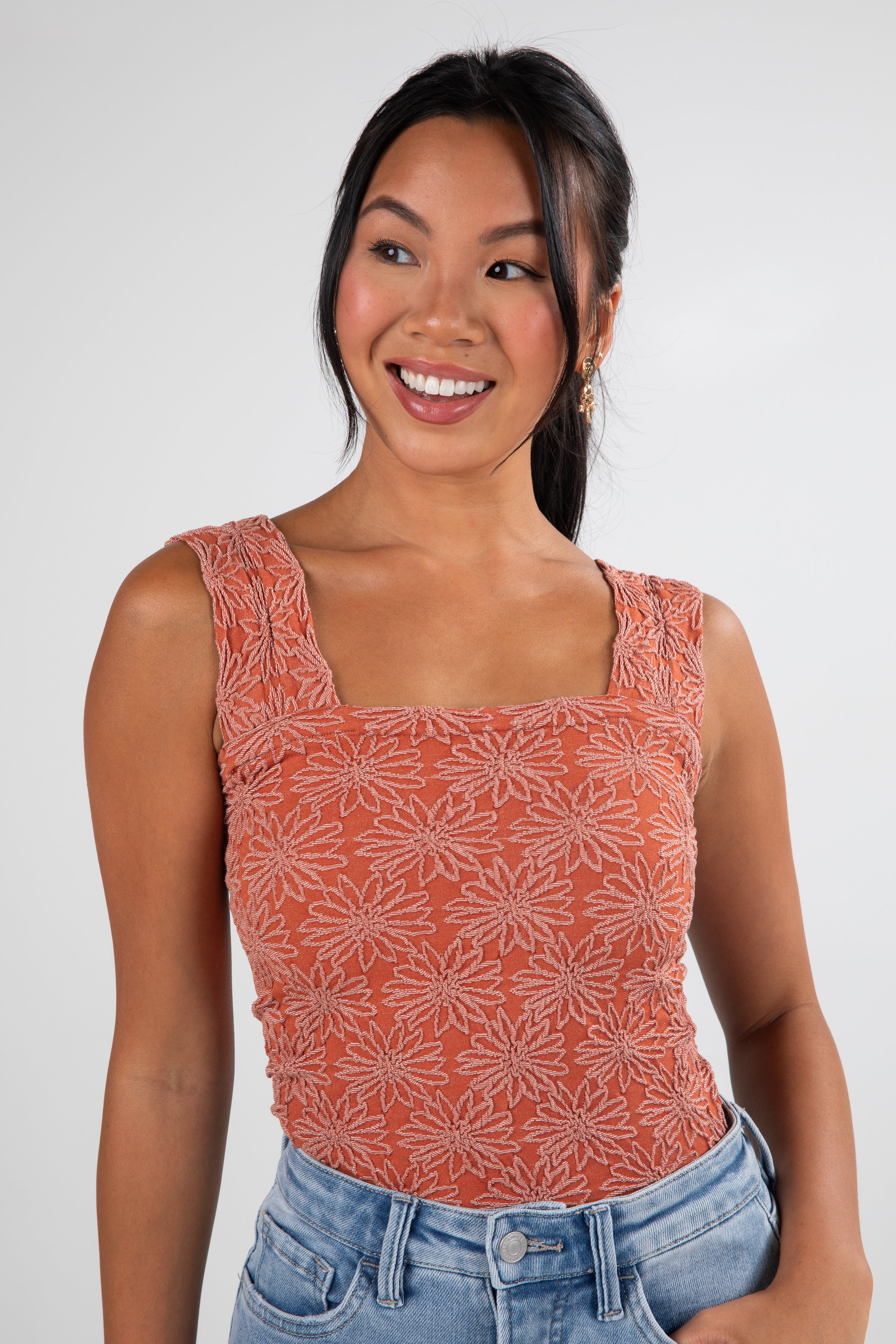 Woman wearing a patterned orange top and blue jeans on a white background