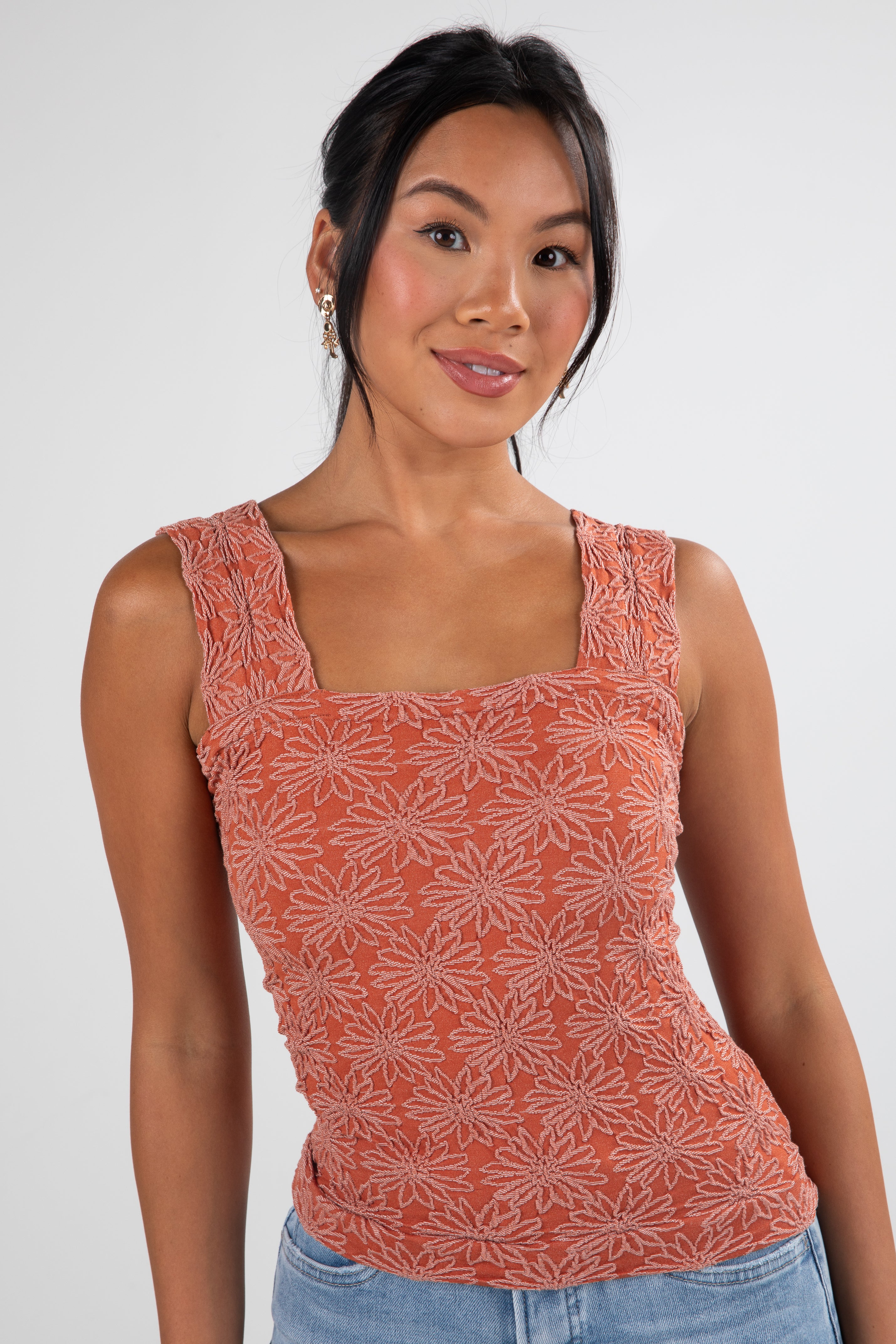 Woman wearing a patterned orange tank top against a white background