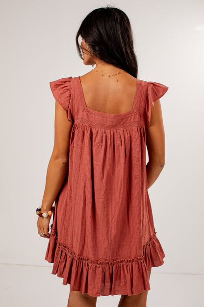 A woman shown from the back wearing a dusty rose ruffled mini dress against a plain white studio background.