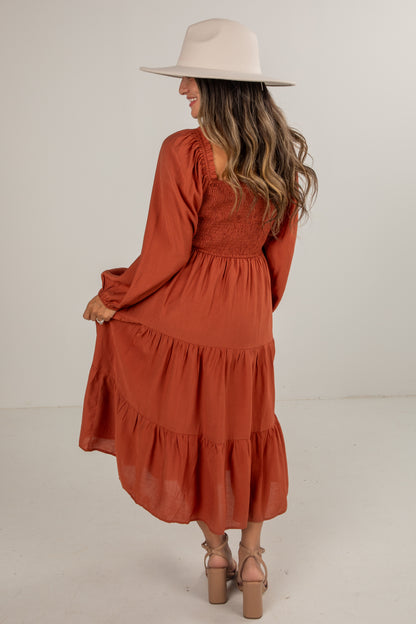 Woman wearing a rust-colored dress and beige hat on a white background