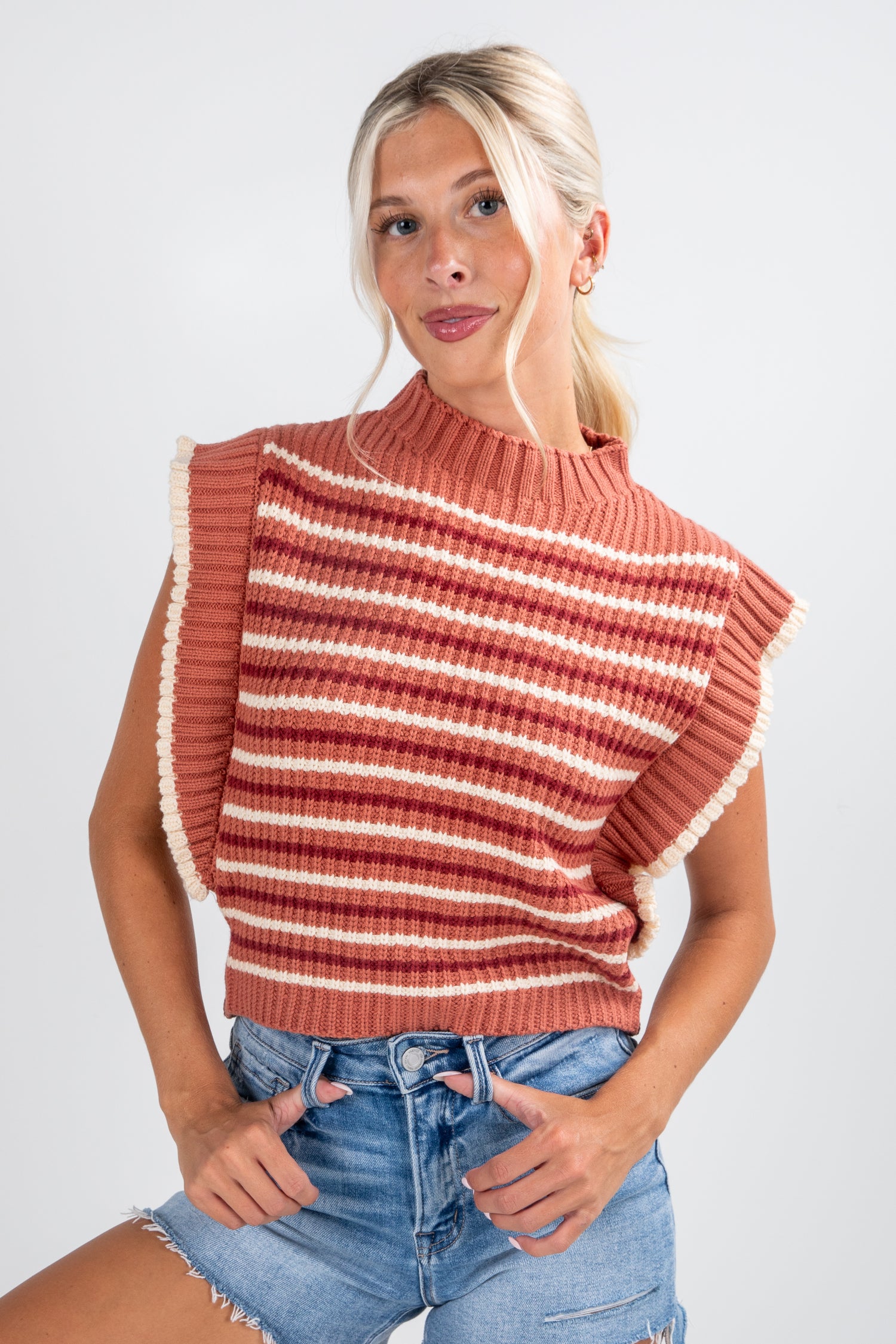 Woman wearing a striped sleeveless sweater and denim shorts on a white background